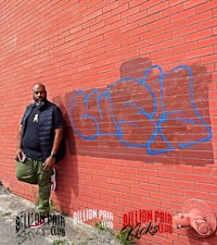 a man standing in front of a red brick wall with graffiti on it